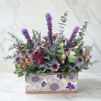 Purple and pink floral arrangement in a patterned rectangular box