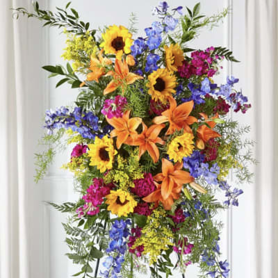 Tall standing floral spray with sunflowers, lilies, and blue flowers