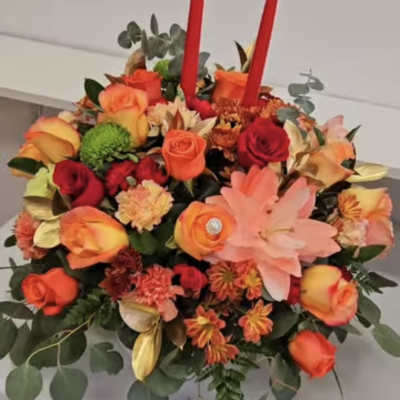 Round floral arrangement with orange and red roses and two red taper candles