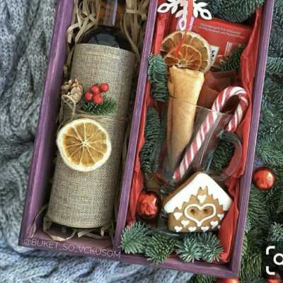 Holiday gift box with a wine bottle, candy cane, cookie, and ornaments