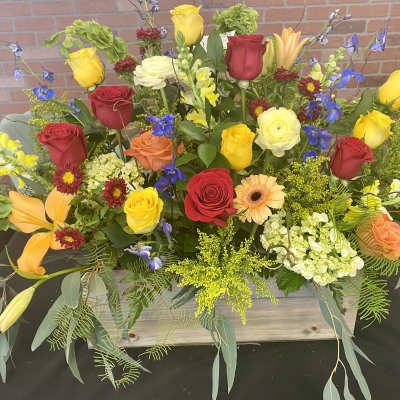 Mixed bouquet of roses, lilies, and other flowers in a wooden container