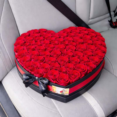 Heart-shaped box filled with red roses and tied with a black ribbon