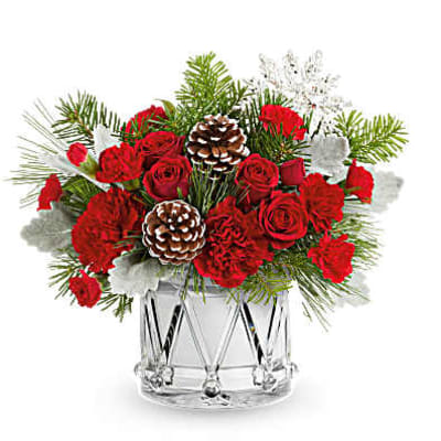 Red roses and carnations in a clear glass vase with pinecones and winter greenery
