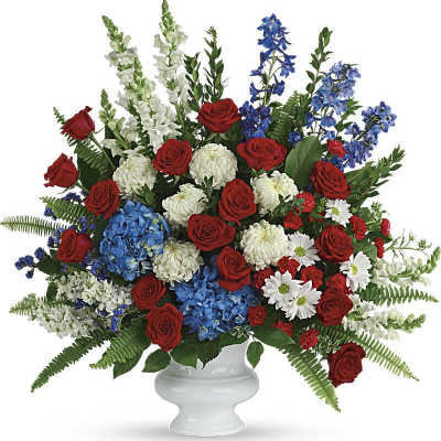 Red roses, blue hydrangeas, and white flowers in a white urn vase