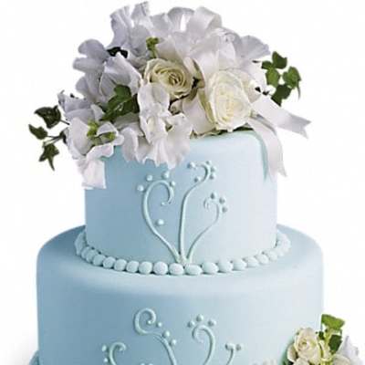 Two-tier blue cake with white floral decorations and ribbon accents