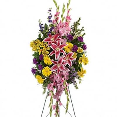 Standing floral spray with pink lilies, yellow daisies, and purple flowers on an easel