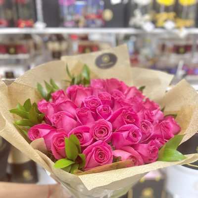 Bouquet of bright pink roses wrapped in tan patterned paper with a black ribbon tie.