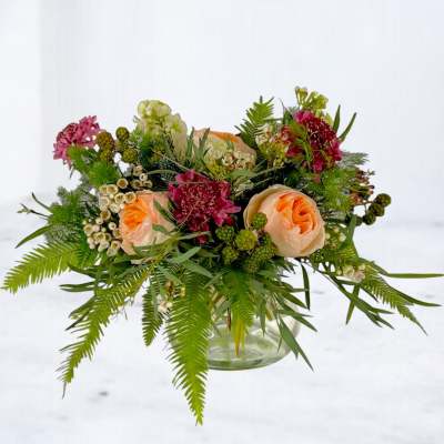 Peach roses and burgundy flowers in a glass vase with fern foliage