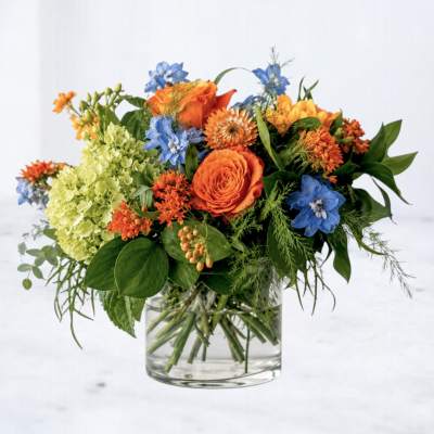 Orange and blue mixed flower arrangement in a clear glass vase