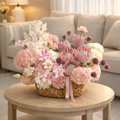 Pink and white floral arrangement in a woven basket on a table
