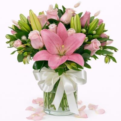 Pink lilies and roses in a glass vase with a white ribbon