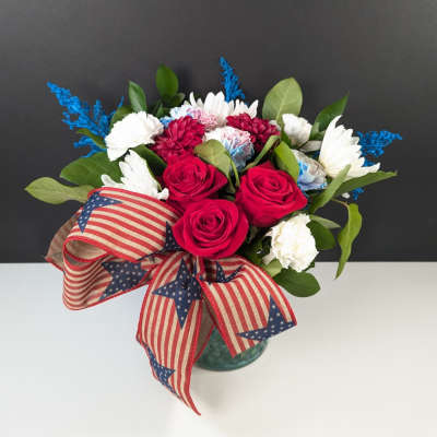 Bouquet of red roses, white daisies, and carnations in a glass vase with patriotic ribbon