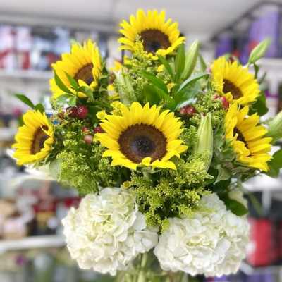 Tall arrangement of yellow sunflowers and white hydrangeas in a clear glass vase
