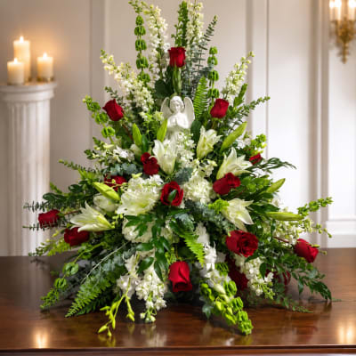 Large floral arrangement with red roses and white lilies around a small angel figurine