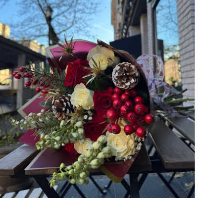 Hand-tied bouquet of red and cream roses with berries and pinecones in burgundy wrapping