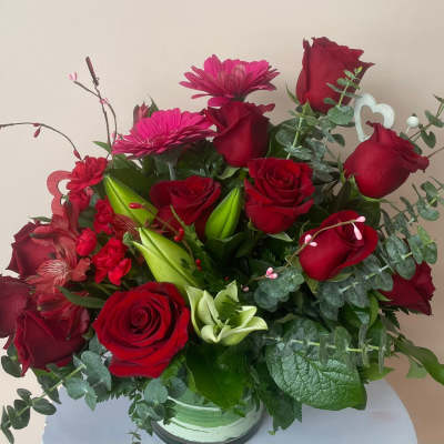 Red rose arrangement with pink gerbera daisies and mixed red blooms in a clear glass vase