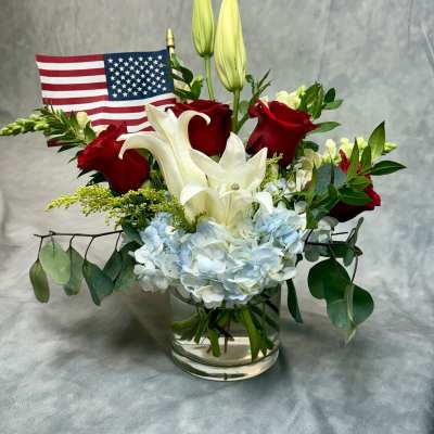 Red roses and white lilies in a glass vase with a small American flag