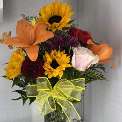 Mixed bouquet with sunflowers, lilies, roses, and a yellow bow in a glass vase