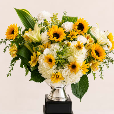 Yellow sunflowers and white flowers in a silver vase on stacked black boxes