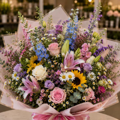 Mixed bouquet with pink roses, lilies, sunflowers, and daisies in pink wrap