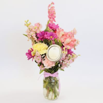 Pink and yellow mixed flowers in a glass mason jar with a ribbon