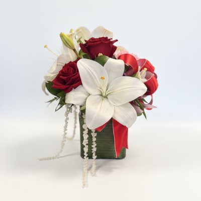 Red roses and white lilies in a green vase with a red ribbon