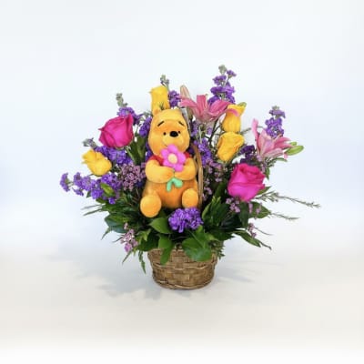 Basket arrangement with a plush Winnie the Pooh toy and colorful flowers