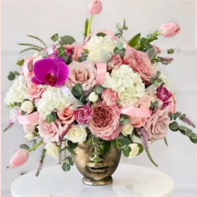 Pink and white floral arrangement in a gold face vase