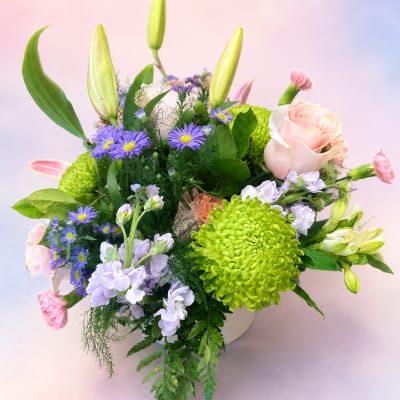 Mixed bouquet with pink roses, lilies, and purple daisies in a white container