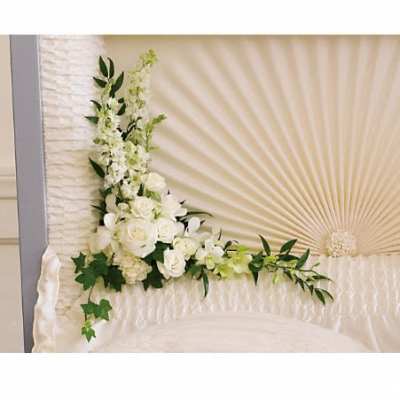 White floral corner spray with roses and other blooms inside a cream casket interior