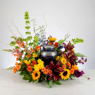 Colorful floral arrangement around a dark urn with sunflowers and roses
