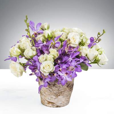White roses and purple orchids in a birch-style container