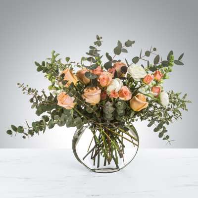 Peach and white roses in a round glass vase with airy eucalyptus