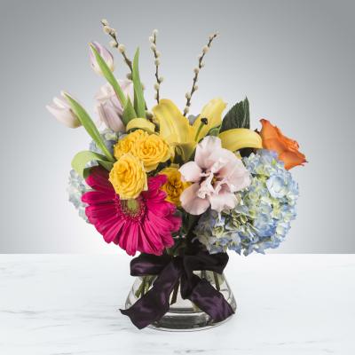 Colorful mixed bouquet in a clear glass vase with a dark ribbon