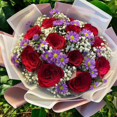 Bouquet of red roses and purple daisies wrapped in pale paper