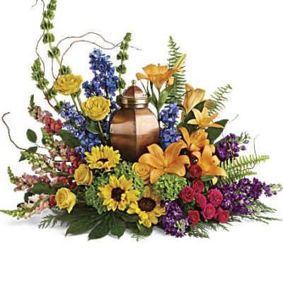 Colorful sympathy arrangement with urn surrounded by yellow lilies, sunflowers, and mixed blooms