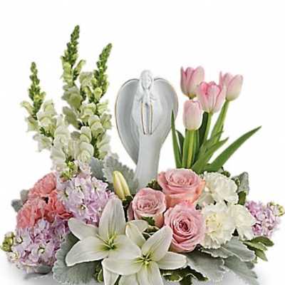 Low pastel arrangement of lilies, roses, tulips, and snapdragons surrounding a white angel figurine