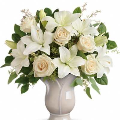Arrangement of white lilies and cream roses in a pale ceramic pedestal vase