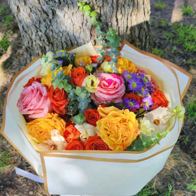 Bouquet of pink, yellow, orange, and purple flowers wrapped in white paper