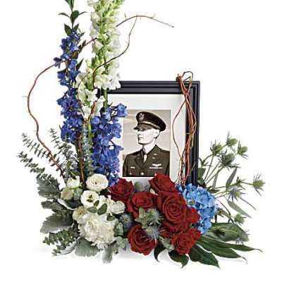 Red, white, and blue floral tribute arranged around a black picture frame with a military portrait.