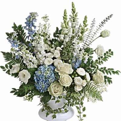 Tall white and blue flower arrangement with roses, hydrangea, and delphinium in a white pedestal vase