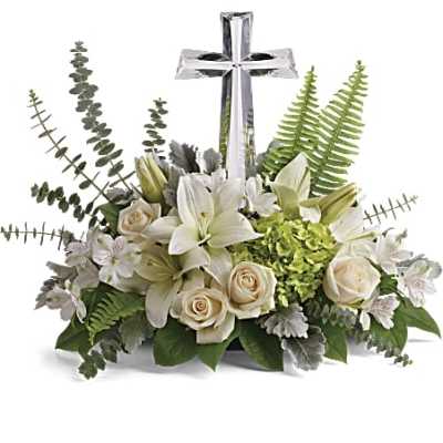 Low white and green floral arrangement with lilies and roses surrounding a clear glass cross.