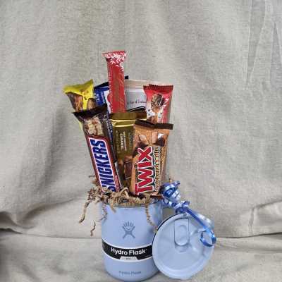 Light blue Hydro Flask mug filled with assorted candy bars and curly ribbon, with matching lid beside it.