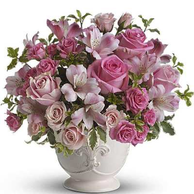 Pink roses and lilies arranged in a white urn vase