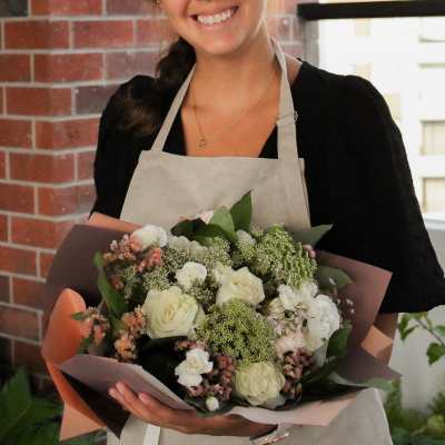 Woman holding a bouquet of cream and blush flowers wrapped in paper