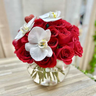 Round arrangement of red roses and white orchids in a clear glass bowl vase.