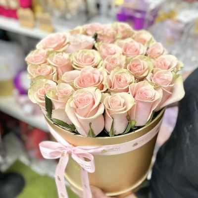 Round gold hat box filled with tightly packed pale pink roses and tied with a pink ribbon.