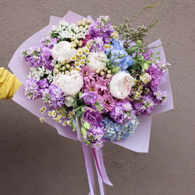 Pastel bouquet with pink, purple, blue, and white flowers wrapped in lavender paper