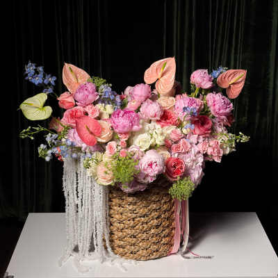 Large pastel floral arrangement in a woven basket with hanging white strands