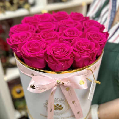 Round white hatbox filled with bright fuchsia roses and tied with a pink ribbon.